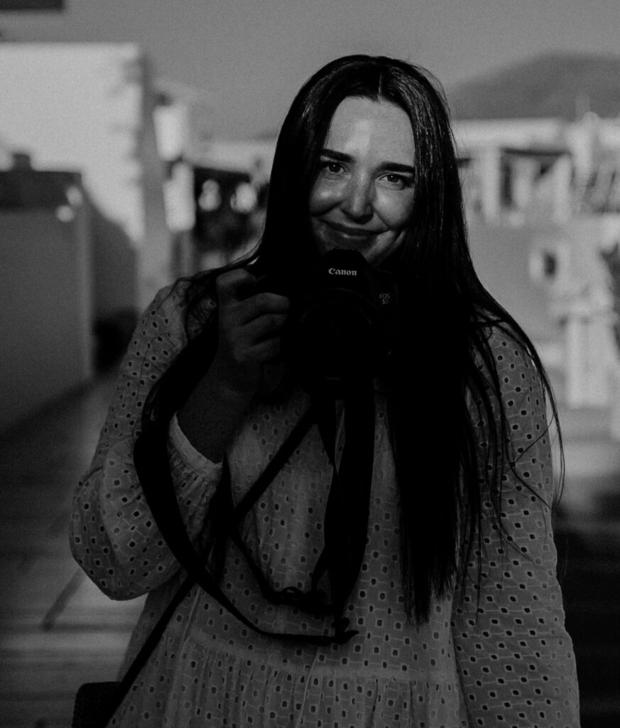 Black and white image of Charlie Hughes photographer smiling holding camera