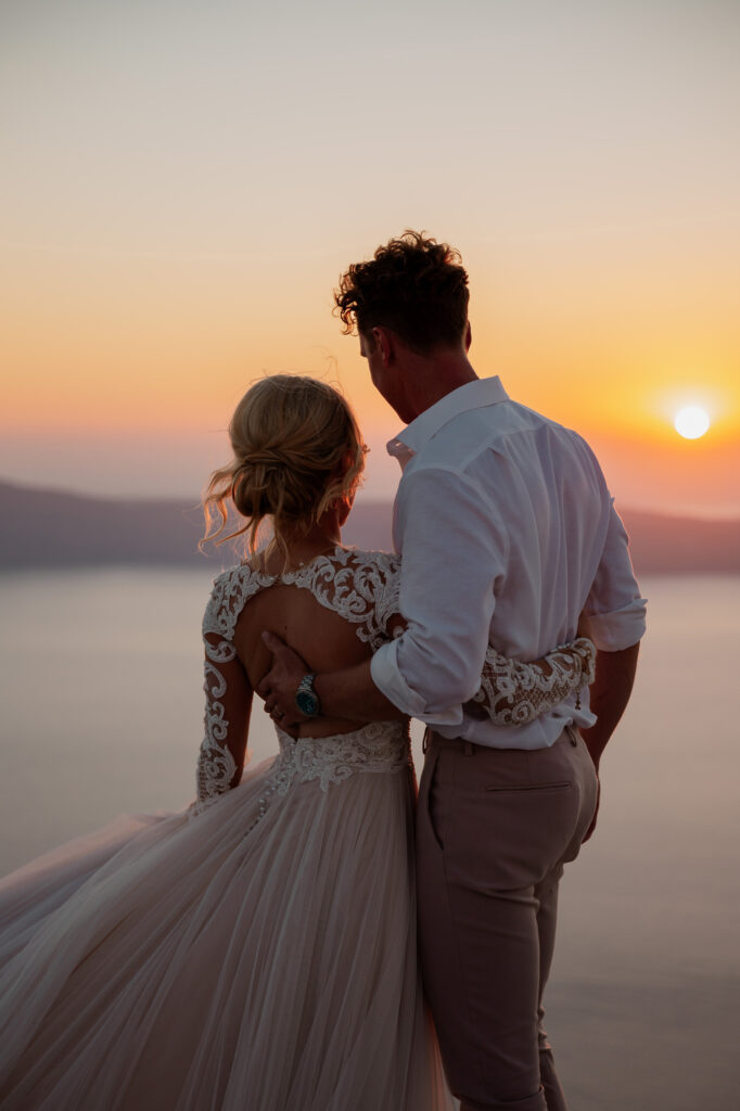 Bride and groom looking out to the caldera in Santorini at sunset.